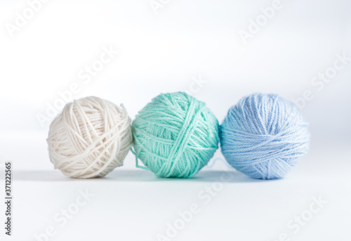 Three balls of yarn lined up on a white surface and white background. Up close view of cream, mint, and light blue colored yarn balls with space for copy above.
