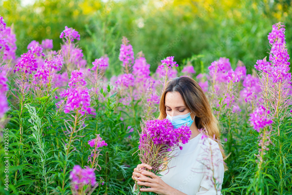 Fototapeta premium A girl in a medical mask sniffs a bouquet of purple flowers in her hands. Spring aggravation of allergies concept. Security measures during the coronavirus pandemic