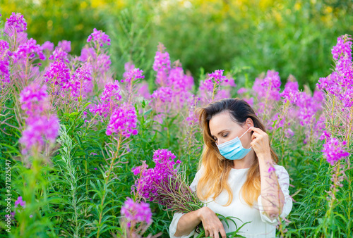 Billede på lærred A girl in a medical mask holds a bouquet of purple flowers in her hands