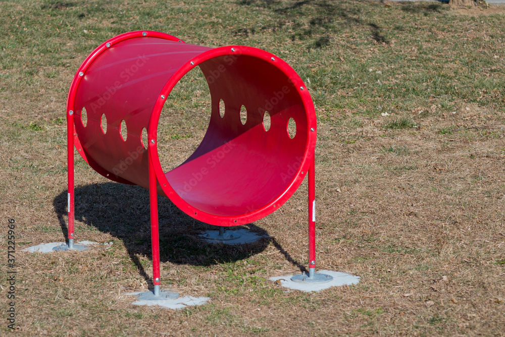 A large red tube made for dog agility courses. The dog runs and jumps through the tube, which is anchored to the ground. A large red tube made for dog agility courses. The dog runs and jumps through the tube, which is anchored to the ground.