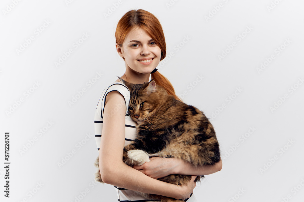 Red-haired woman holds in her hand a cat striped T-shirt light background home pet