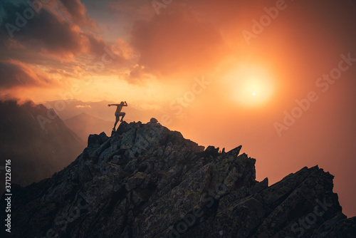 Sport photo in mountains. Silhouette of runner on the top of the hill, orange sunset sky in background. Edit space.