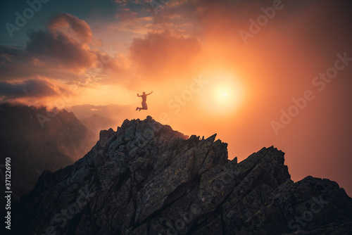 Silhouette of young man jumping and arm up on top of mountain, sky and sun light background. Business, success, leadership, achievement and people concept..