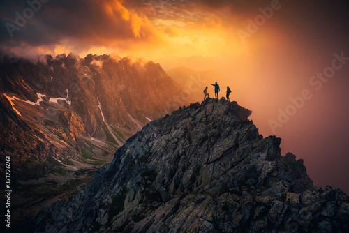 Team success concept photo  friends standing together on the top of the hill  over beautiful mountains landscape in gold sunset light  orange edit space..