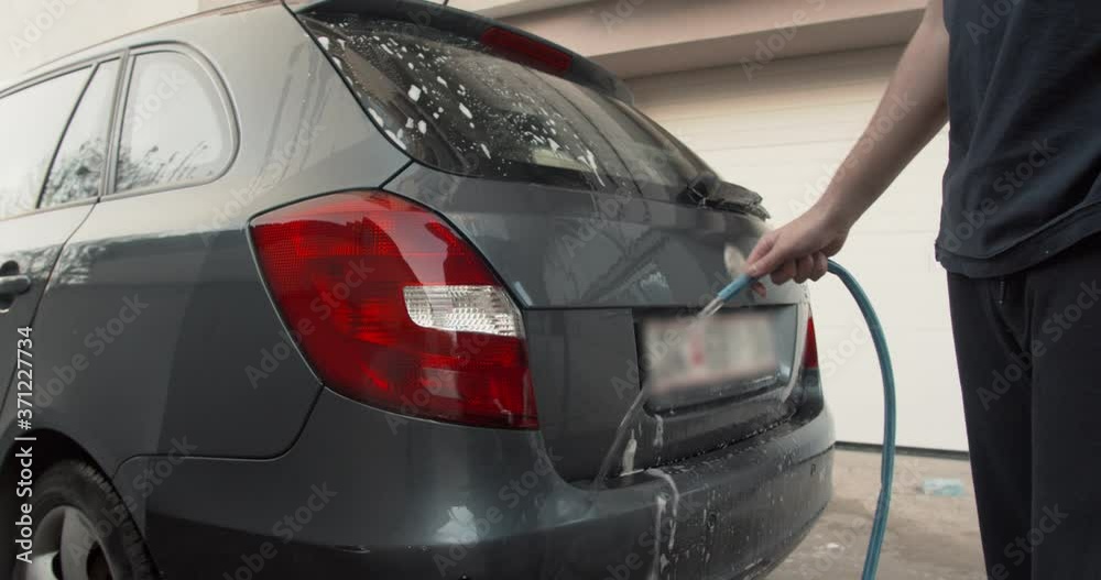 Boy washing the family car with a hose and running water Boy washing the family car with a hose and running water