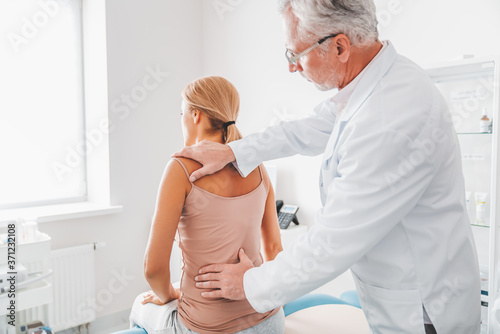 Mature male orthopedist in eyeglasses examining female patient's back in clinic photo