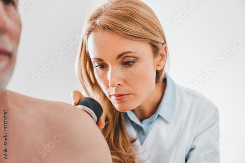 Female dermatologist examines skin moles or acne of senior patient with dermatoscope