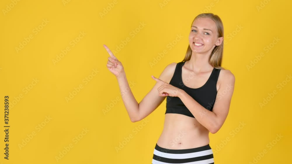 Young fit blonde girl in sportswear smiles and shows copy space. empty place for promotional image. studio shot isolated on yellow background. Young fit blonde girl in sportswear smiles and shows copy space. empty place for promotional image. studio shot isolated on yellow background.