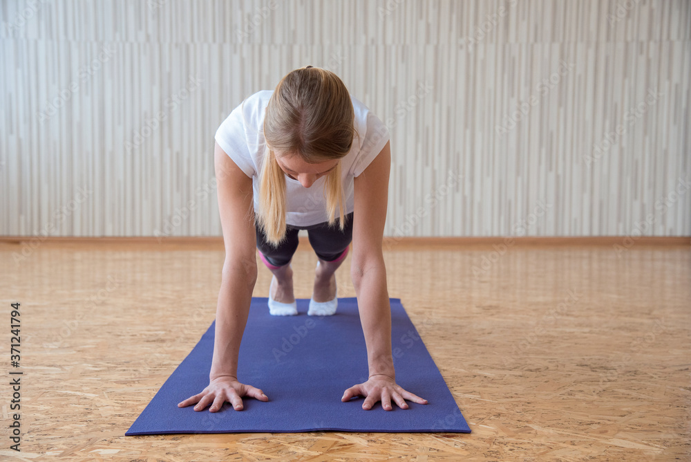 The girl practices yoga in the gym and stands on the arms in the plank