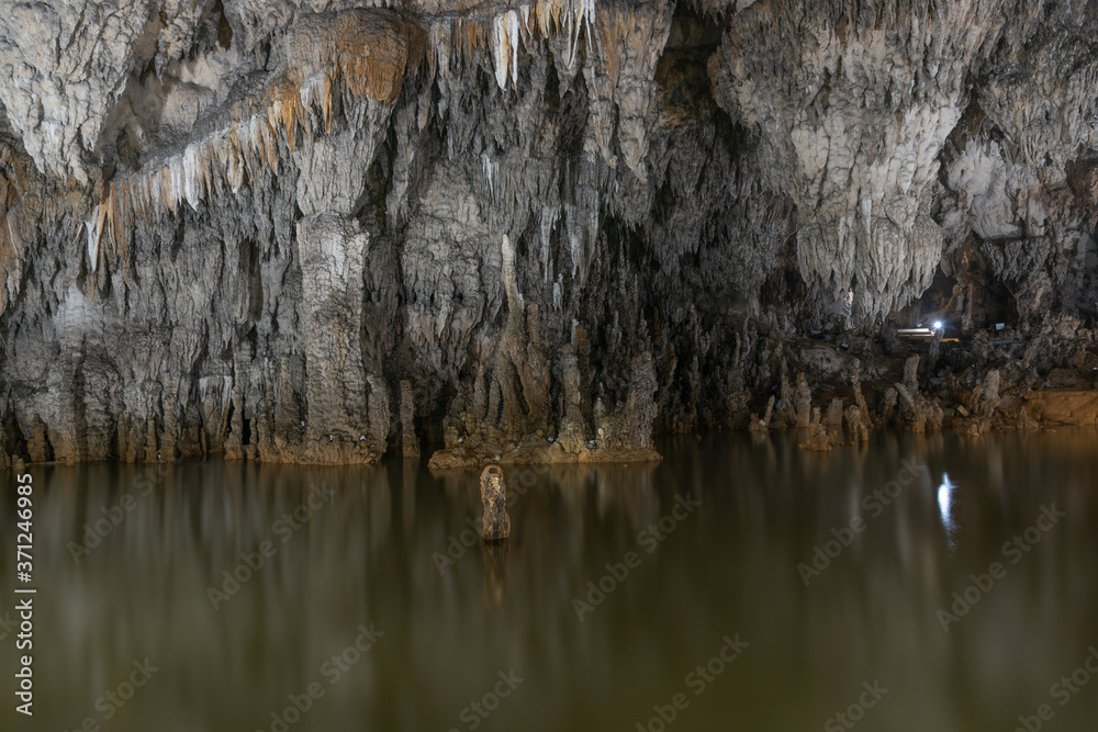 Obraz premium Grey rock stalactite wall and water in the cave