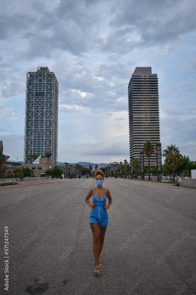 Young woman walking through the empty city of Barcelona wearing a face mask
