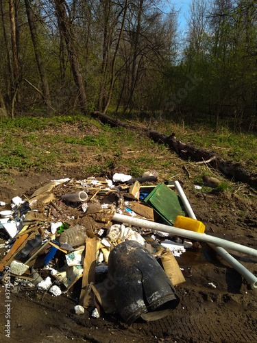 A huge mountain of household waste lies on the road in a green, blooming forest.