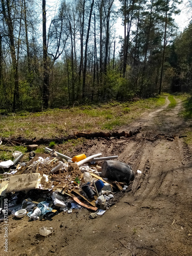 A huge mountain of household waste lies on the road in a green  blooming forest.