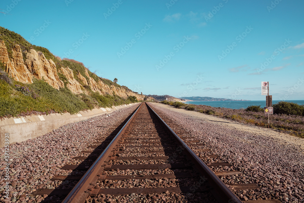 A railroad track along the beach and ocean on a sunny afternoon.

