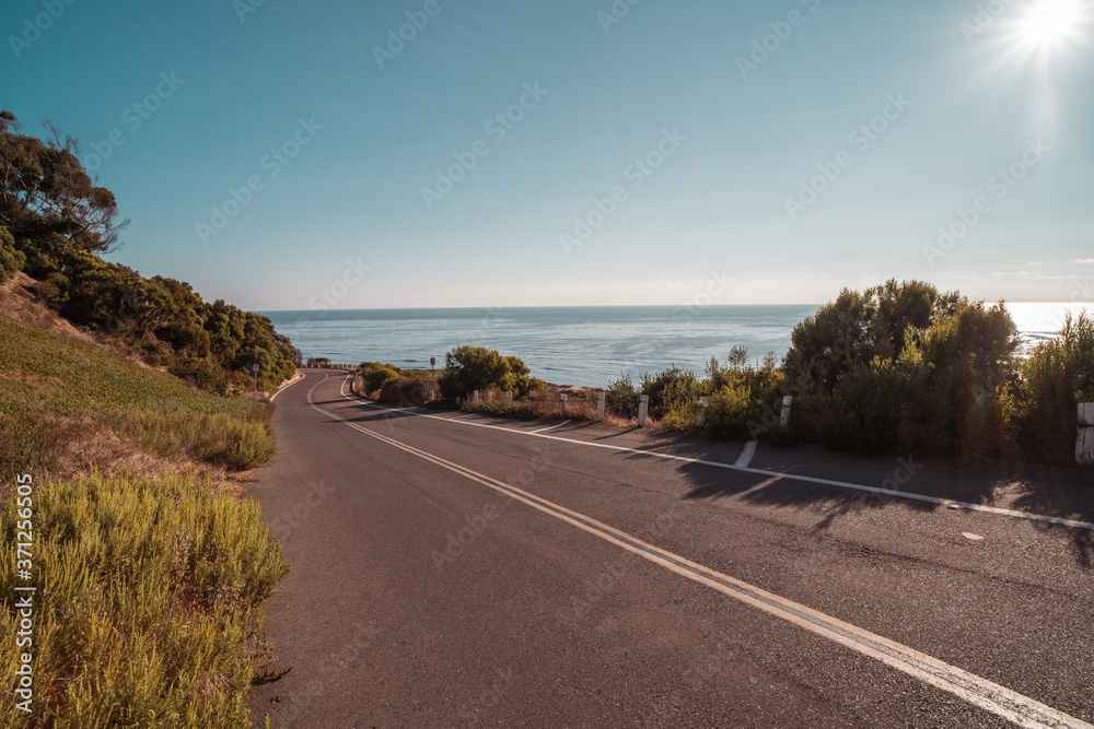 An empty road leading toward the beach and ocean on a sunny afternoon.