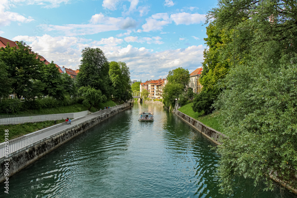 A tourist boat travelling along the Ljublijanica River in afternoon in Ljubljana A tourist boat travelling along the Ljublijanica River in afternoon in Ljubljana