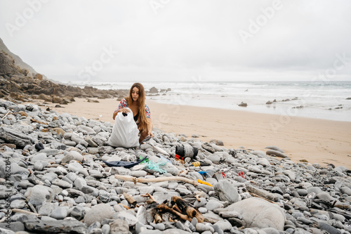 Young girl picking up plastic waste from beach photo