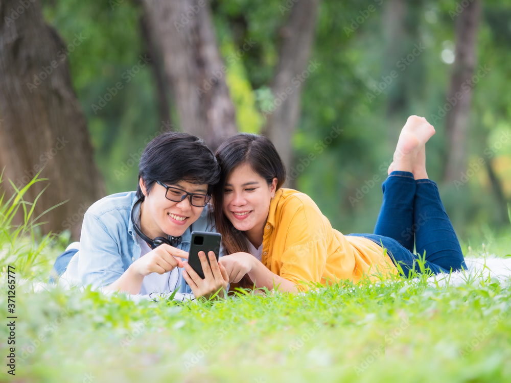 Asian LGBT couples relax in the park while listening to music on their mobile phones Asian LGBT couples relax in the park while listening to music on their mobile phones