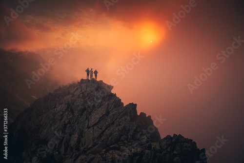 Team success concept photo, friends standing together on the top of the hill, over beautiful mountains landscape in gold sunset light, orange edit space..