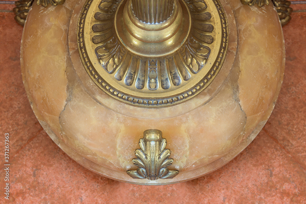 A decorated marble base of a bronze vintage lamp on a stone tile.