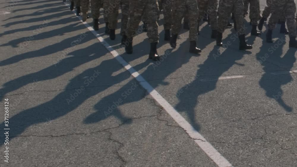 Soldiers marching down city streets, wearing camouflage uniforms. Low angle view of their legs and feet as the march by.