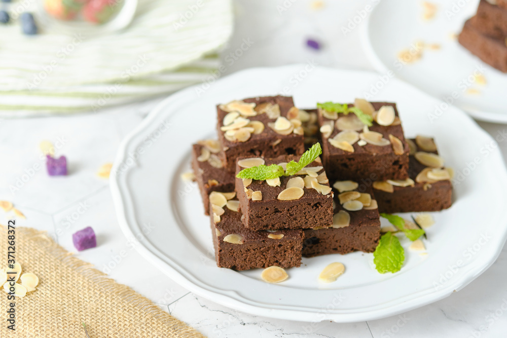 Squares Chocolate brownie with almond sliced set on white cafe table.