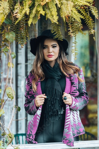 Beautiful model posing for photos on the street. Wearing black pants, purple blouse and hat. 