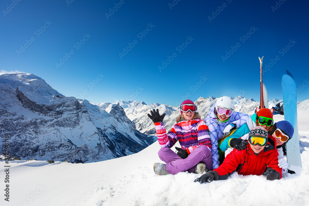 Group of happy young adults lay in snow wave hands with snowboards over mountain peaks