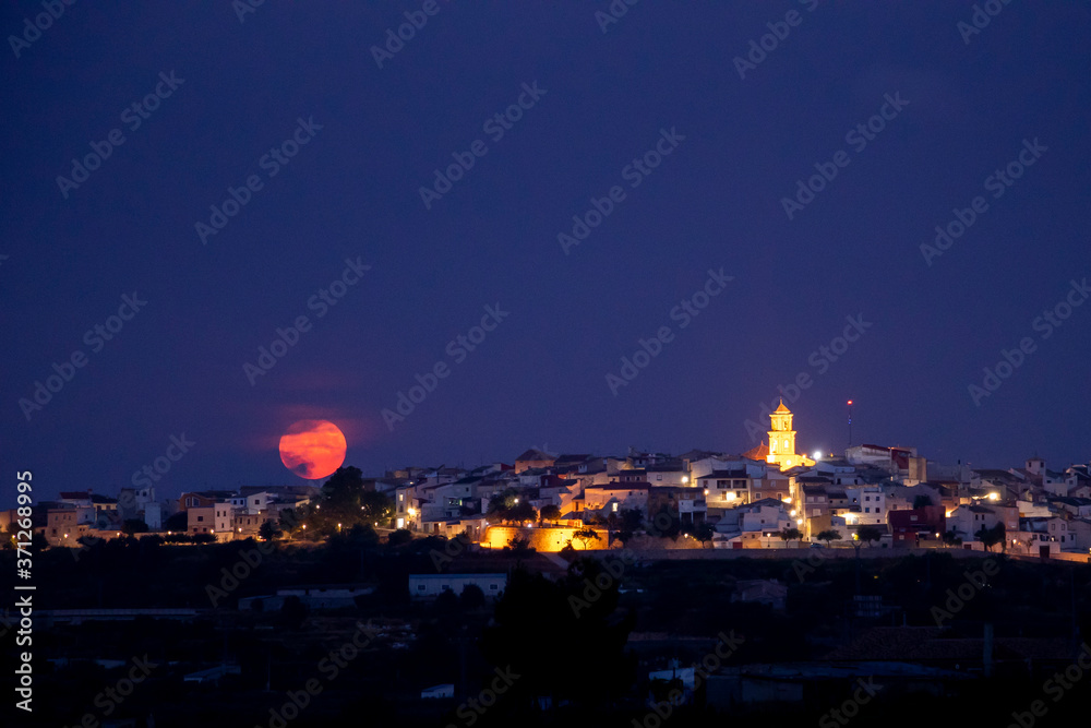 full moon rising over the horizon of a town