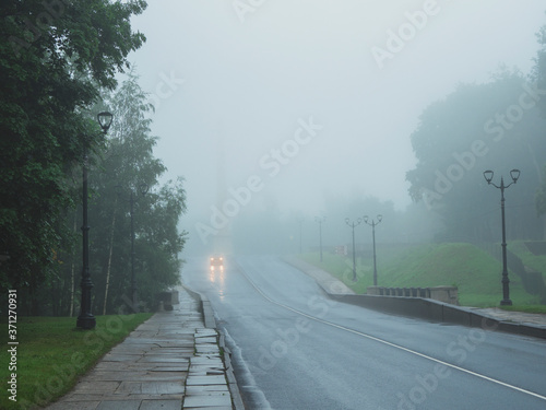 A car with its lights on on a foggy road on a cold morning