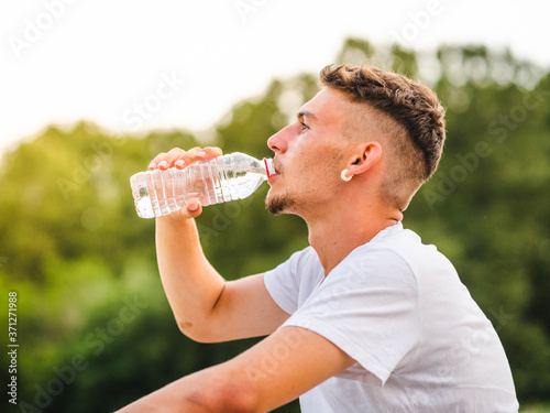 Shallow focus shot of a Caucasian male drinking water after a workout in a park