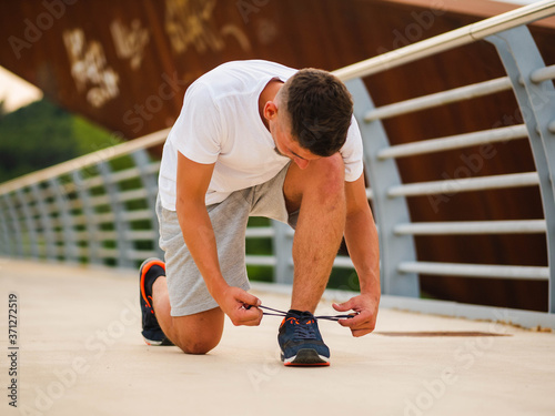 Young attractive sportsman tying shoelaces during his morning run
