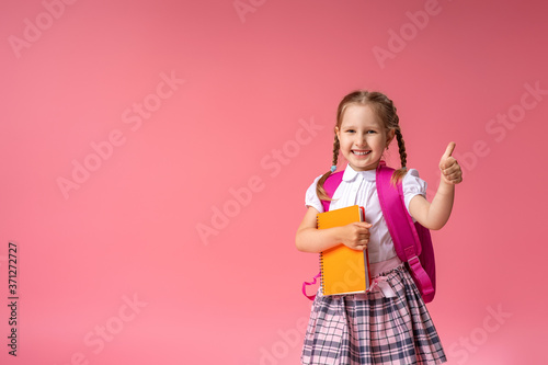 little girl with a backpack and a book gives a thumbs-up sign of approval.