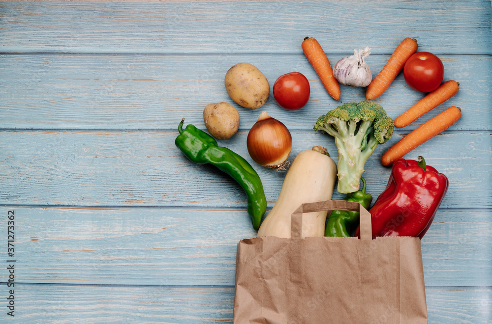 assortment of fruits and vegetables spilling out of a paper bag on blue background