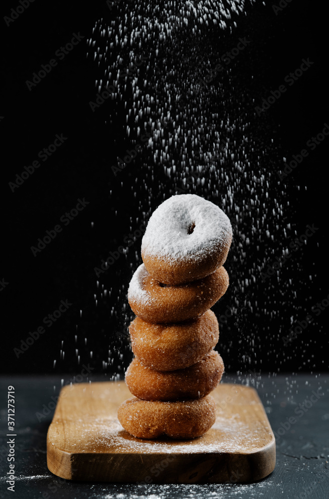 donuts forming a tower applying glass sugar on black background