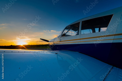 Close-up of a small parked plane with a propeller against the backdrop of a sunset.