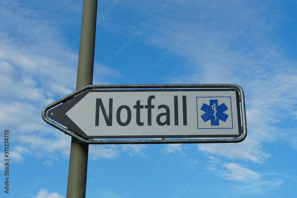 Fototapeta premium A shield or sign showing a emergency room, ER, in German language on the background of blue sky and cirrus clouds