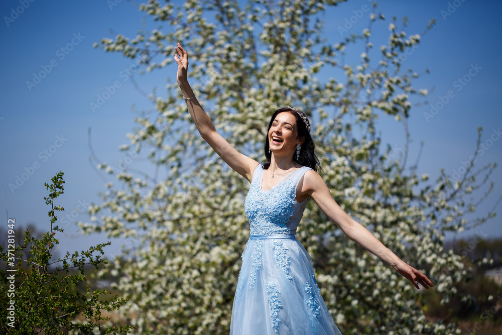 Young woman with beautiful make-up with a vintage hoop in a blue light dress with a bouquet posing on a background of green foliage in a park. Fresh portrait attractive girl with white flowers. Young woman with beautiful make-up with a vintage hoop in a blue light dress with a bouquet posing on a background of green foliage in a park. Fresh portrait attractive girl with white flowers.