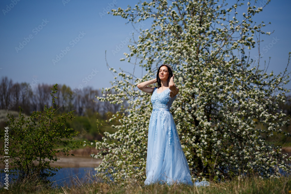 Portrait of a tender girl in a blue long dress with tulle under blooming cherry with a smile on her face on a sunny warm summer day Portrait of a tender girl in a blue long dress with tulle under blooming cherry with a smile on her face on a sunny warm summer day