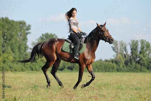 Beautiful young woman riding a horse on the summer field © horsemen