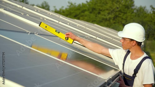 Young enginneer installing new sunny batteries. Worker in a uniform and hardhat installing photovoltaic panels on a solar farm. The green energy concept photo