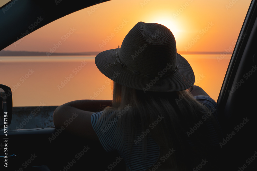 Φωτογραφία A young woman looks out the car window at the sunset on the sea.