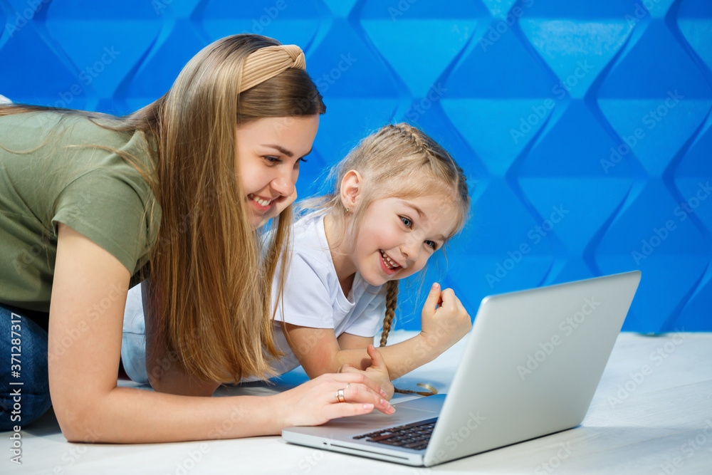 Cute little girl looking ready to use the laptop keyboard while sitting on the kitchen floor with her loving mother