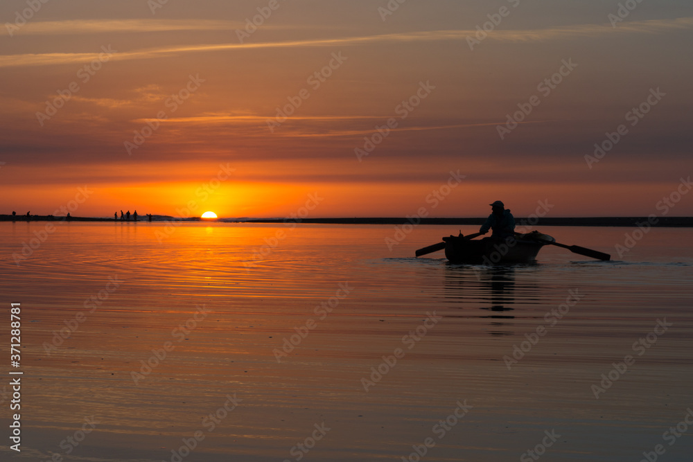 Young man fishing on a river from the wooden boat  at sunset . A fisherman in an old wooden boat rowing in the river at sunset