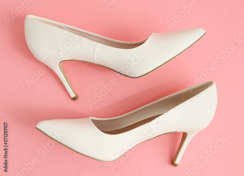 pair of white shoes One pair of white high-heeled shoes lie on a pink background, top view close-up.