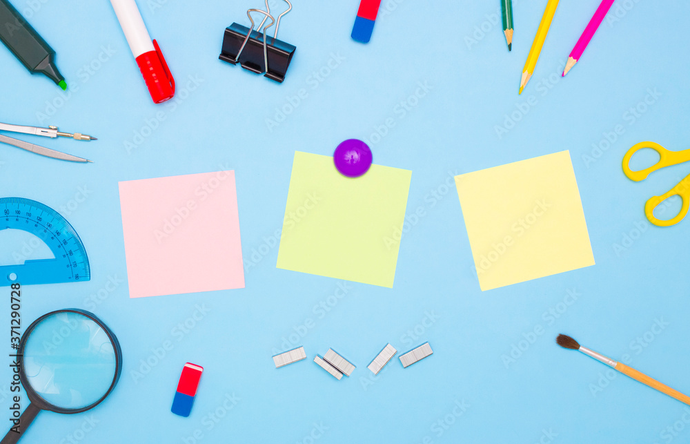 The concept of school and students. Three empty square of colored paper for notes in the middle. School and office stationery on the edges on a blue background. Top view, free space for text. The concept of school and students. Three empty square of colored paper for notes in the middle. School and office stationery on the edges on a blue background. Top view, free space for text.