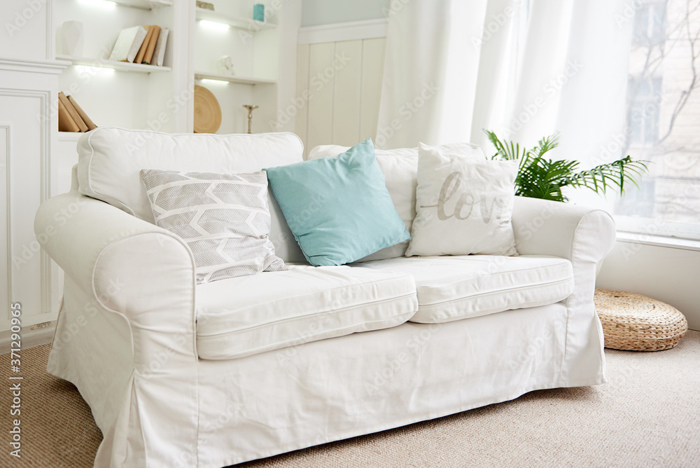 Fototapeta premium Stylish interior design with white sofa, cushions and tropical palm plant in pot, copy space. Couch decorated with pillows and houseplant at home