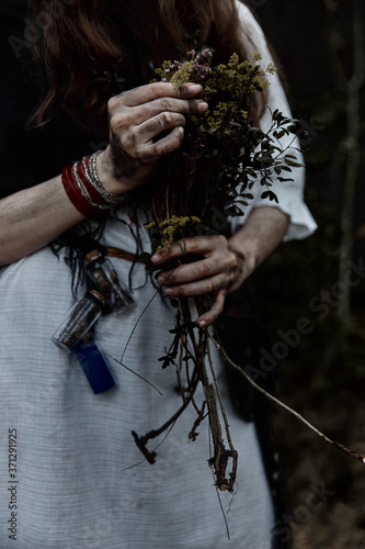 Woman in white witch dress holds dry herbs for witchcraft and potions. Horror themes. Halloween.