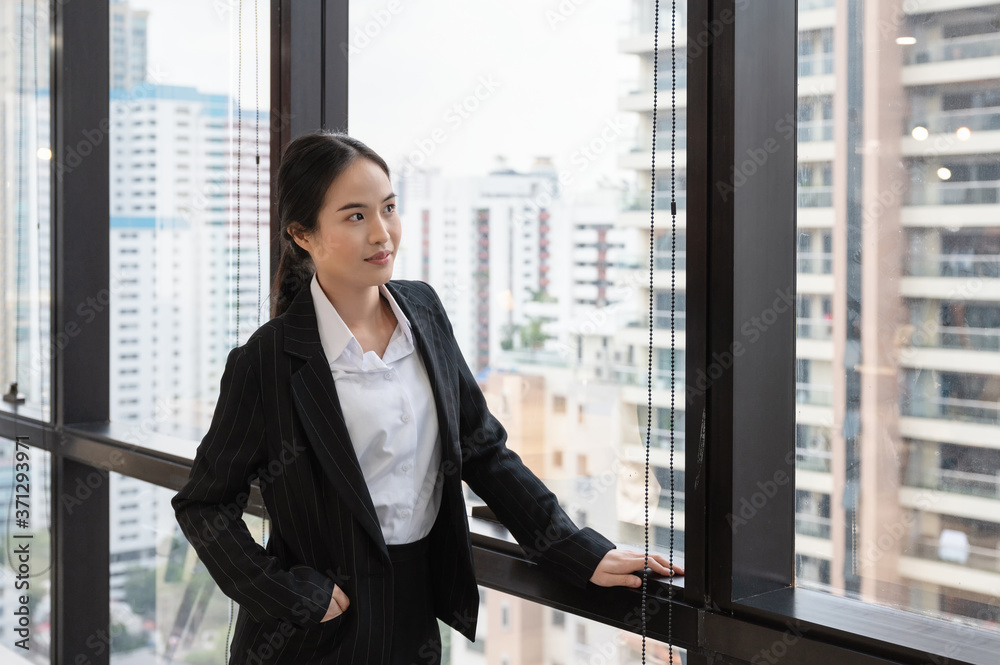 Young asian businesswoman standing and looking through window on office building Young asian businesswoman standing and looking through window on office building