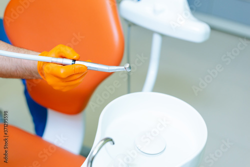 Mele dentist's hand in orange glove holding dental drill